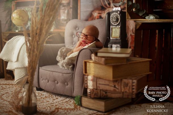 Ein Baby liegt in einer nostalgisch anmutenden Umgebung auf einem kleinen Sofa, schlafend. Es trägt ein große Brille. Im Vordergrund ist ein altes Radio im Hintergrund ein Globus zu sehen.