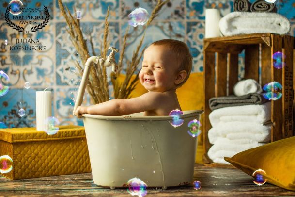 Ein Baby sitzt in einer kleinen Wanne voll Wasser und hat Spaß beim Baden. Im Hintergrund Badezimmerdekorationen.