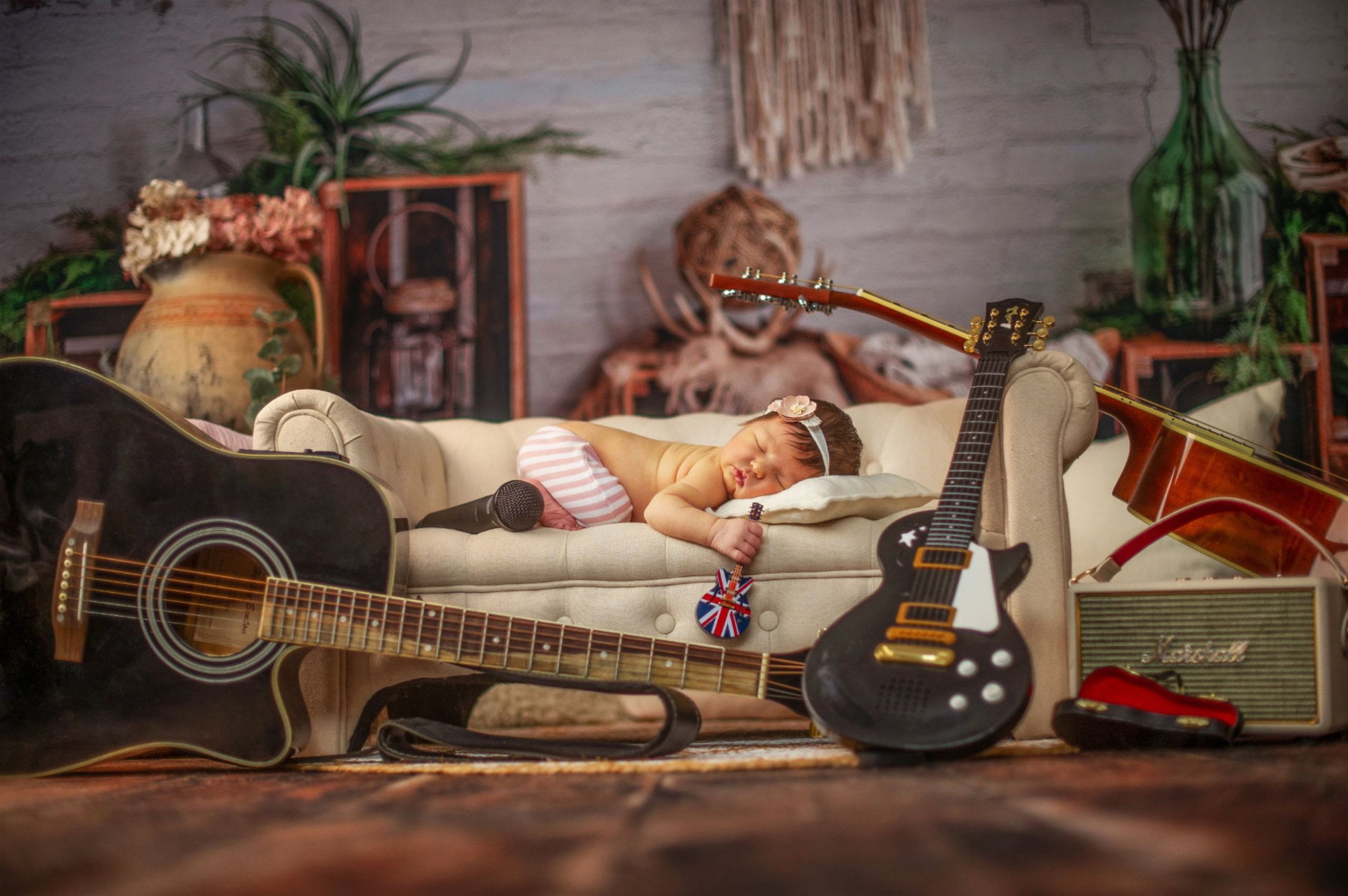 Baby liegt auf einem Sofa und hält eine Mini-Guitarre in der Hand. Ringsherum liegen weitere Guitarren.