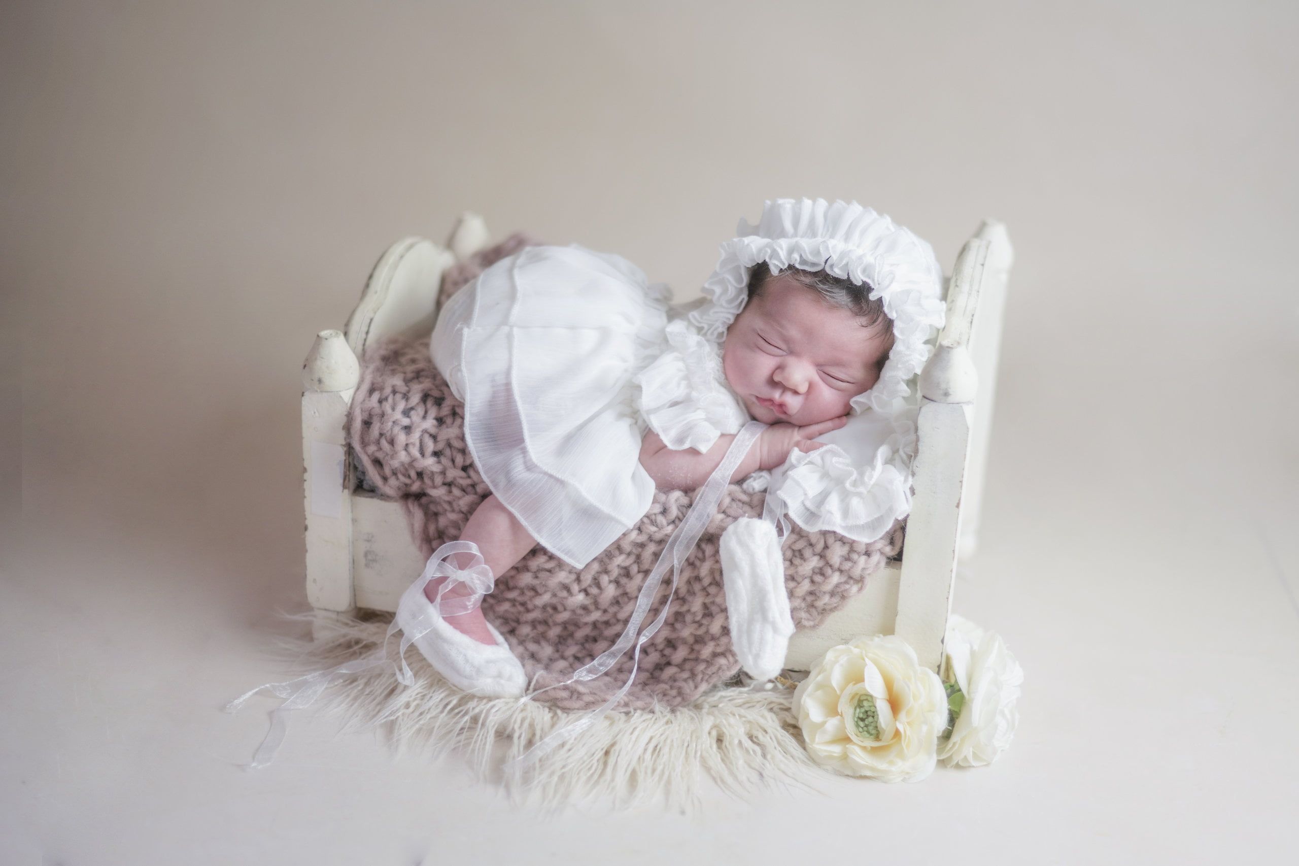 Babyfotografie Hamburg. Ein kleines Baby liegt in einem kleinen Bettchen. Es trägt ein weißes Kleidchen und lässt einen Fuss aus dem Bett hängen.