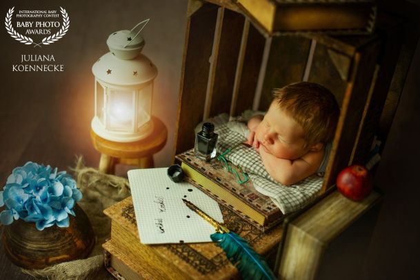 Ein Baby ist auf einem Bücherstapel eingeschlafen. Vor ihm liegt ein Tintenstift. Daneben leuchtet eine kleine Laterne.