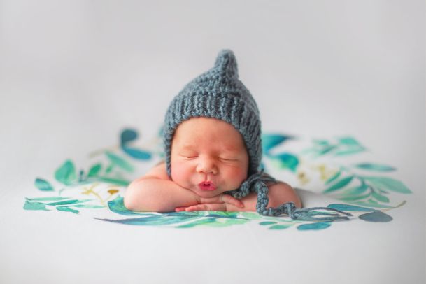 Baby lies prone with a cap on his head and sleeps with a kissing mouth.