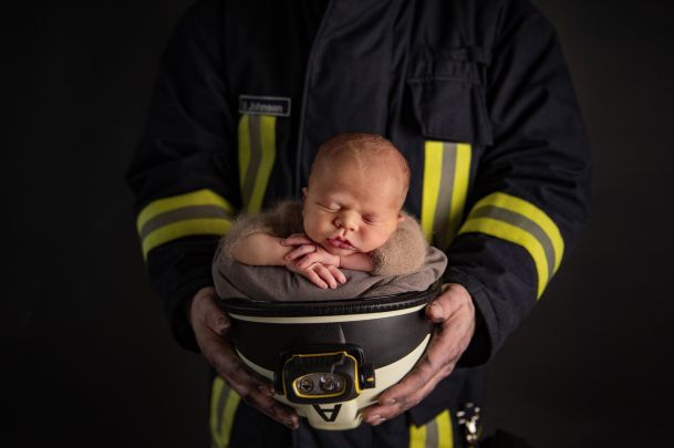 A firefighter holds his helmet upside down in his hands, in which the newborn baby is sitting