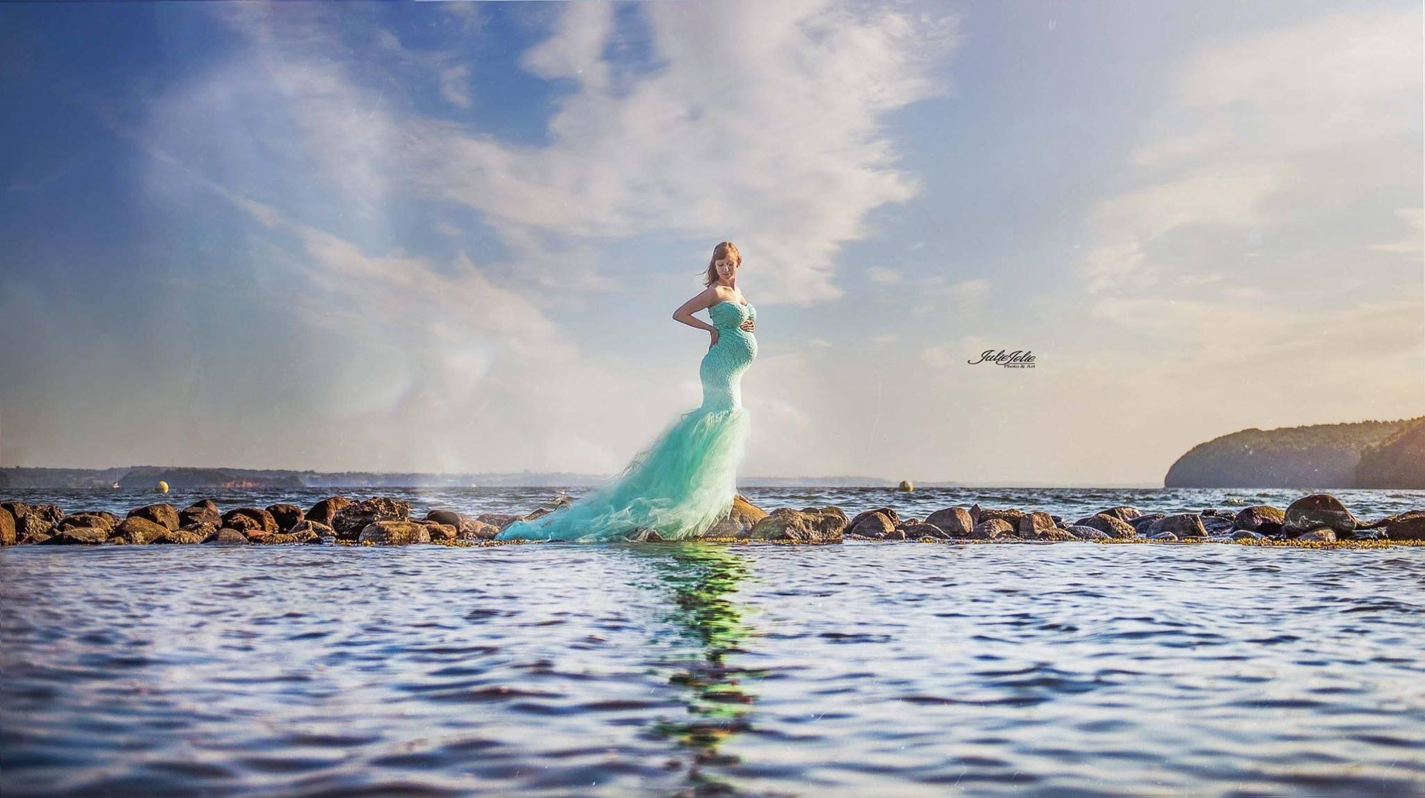 Babybauch Shooting am Strand. Das Bild zeigt eine schwangere Frau in grünem Kleid, die am Strand steht.