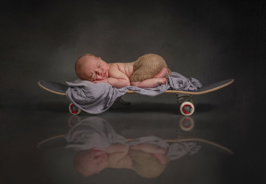 Babyfotografie mit Skateboard. Ein Baby liegt schlafen auf einem Skateboard.