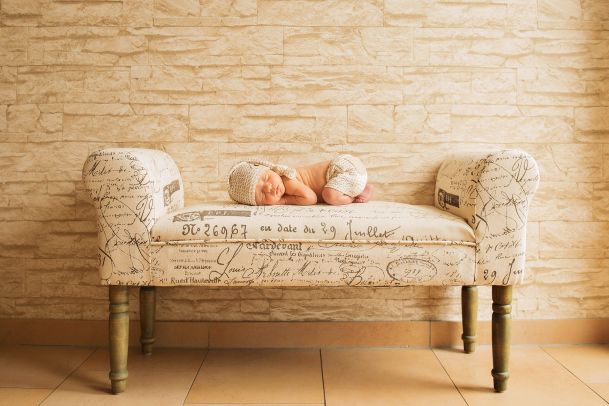 A prone baby, legs drawn up, asleep on a cream-colored divan. In the background a cream-colored wall.