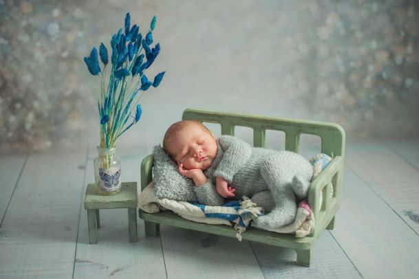 Baby lies on a small bench and sleeps. Next to it is a small bedside table with blue flowers.