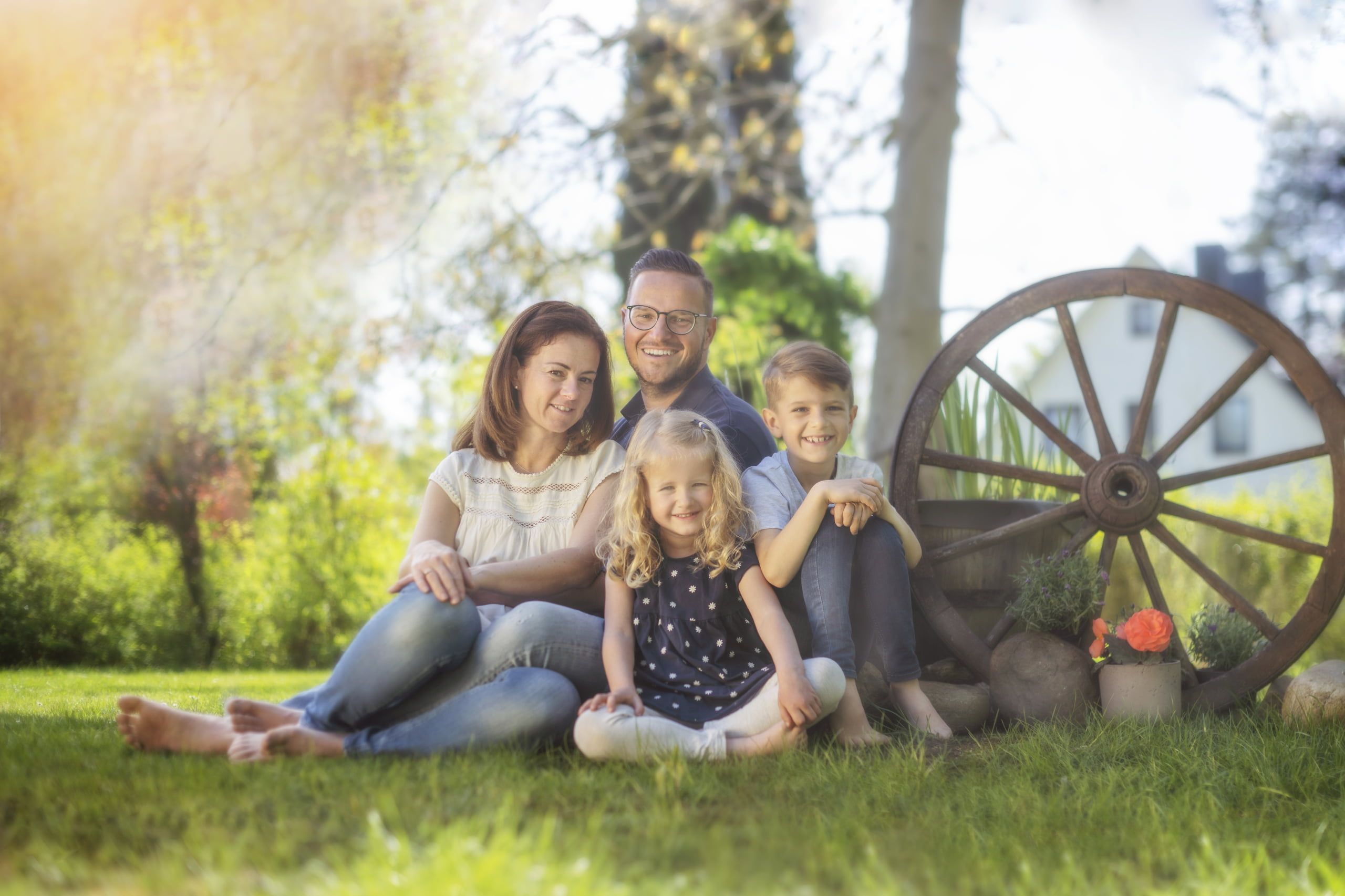 Julie Jolie Familienfotografie. Eine Familie sitz zusammen auf dem Rasen. Rechts daneben ein altes Wagenrad.