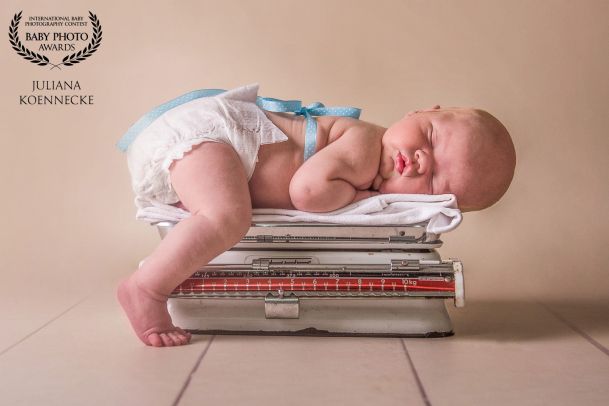 Ein Baby liegt in Bauchlage, schlafend auf einer medizinischen Waage. Ein Fuß berührt dabei den Boden, als würde es sich abstützen.